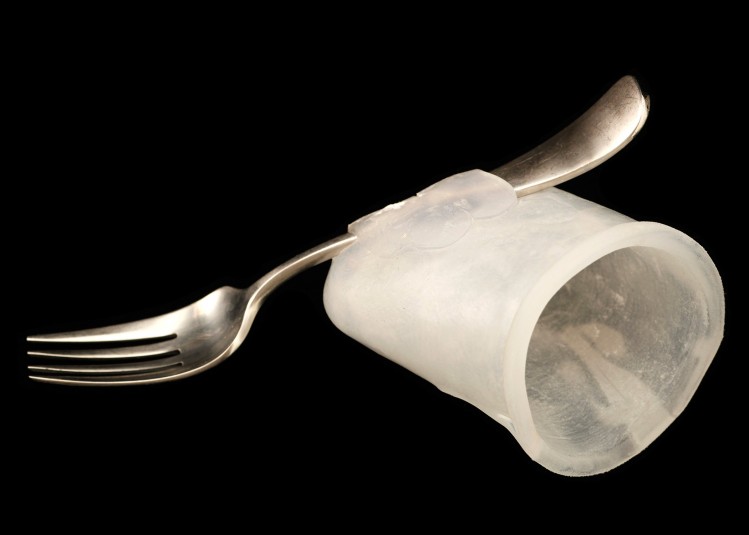 Studio shot of the fork/silicone unit, showing the silicone cap's hollow opening from a slightly side angle. The entire front side of the silver fork is visible resting across the silicone cap.