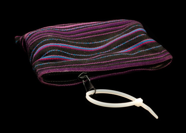 A studio shot of a white plastic cable tie looping through the zipper pull of a small woven handbag. The tie's large loop make it easier to grab and pull than the tiny zipper.