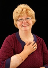 Headshot of Cindy smiling with right cosmetic hand placed on her chest, above her heart.