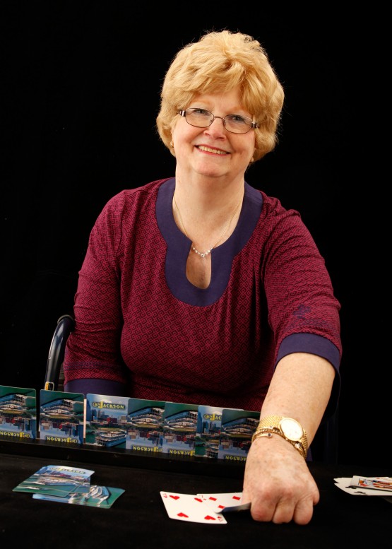 Cindy smiling at camera and reaching to play a card on the table in front of the card holder.