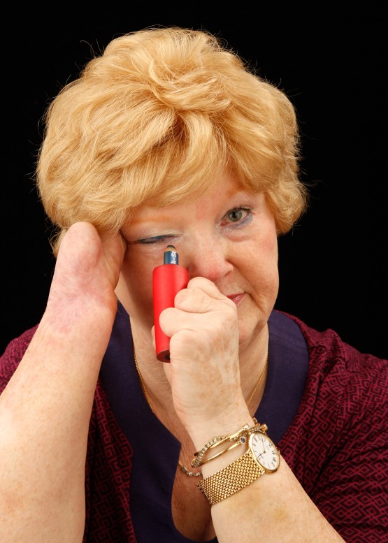 Cindy looks at the camera as though in a mirror, holds her right eye taut with her right hand, and applies eyeliner with her left.