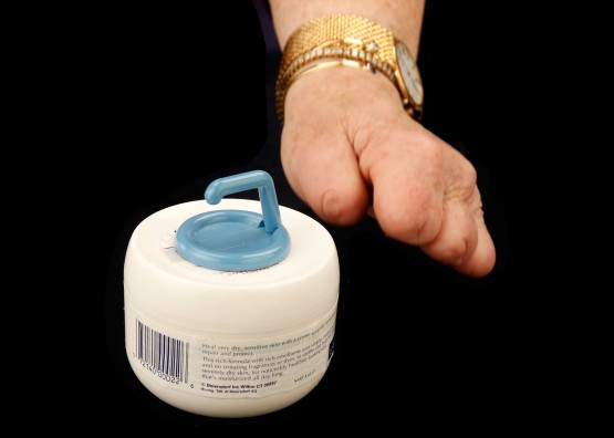 Cindy's hand reaching to grasp the blue adhesive hook on the cold cream jar.