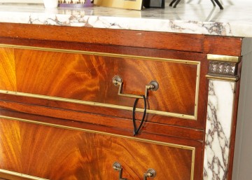 A shot of a wood and marble bureau with a cable tie hanging from the brass drawer pulls.