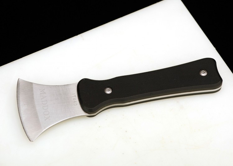 Stainless steel rocker knife with a black handle, lying on a white cutting board. The brand name of the rocker knife is visible, 