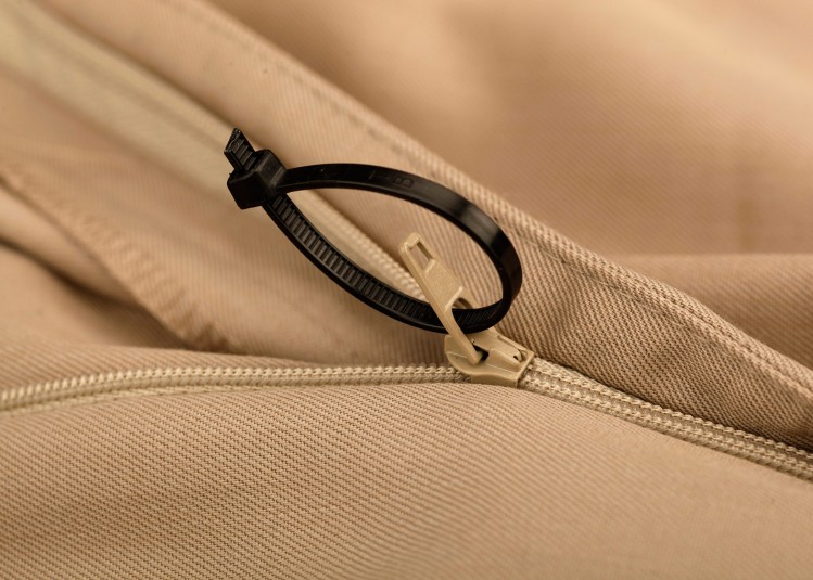 A small black plastic cable tie makes the zipper accessible on a pair of pants.